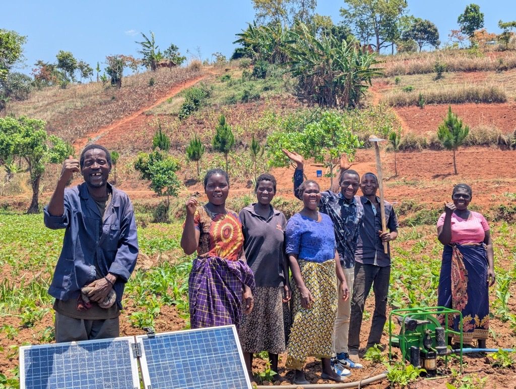 A farming co-operative standing beside their solar-powered irrigation pump on a replanted hillside